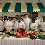 Group of culinary students posing behind a beautiful spread of food