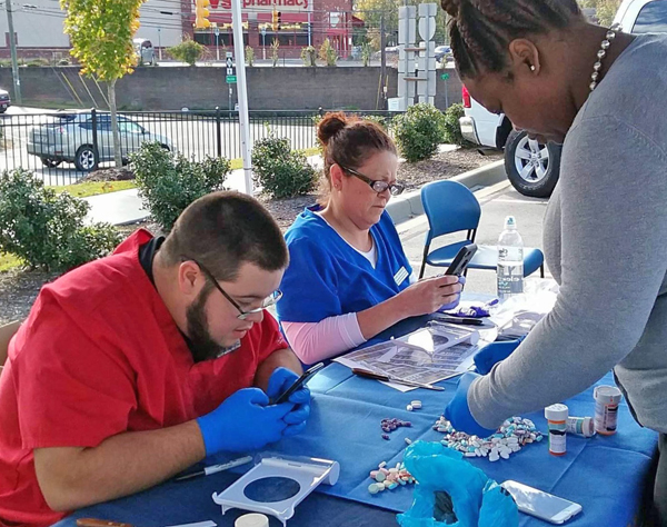 Seated, from left, VGCC Pharmacy Technology students Tommy L. Hicks of Franklinton and Malissa S. Chandler of Durham use smartphones to identify and classify medications while Pharmacy Technology program head Dr. Erica Fleming (standing at right) sorts through medications during the “Operation Medicine Drop” event at Walgreens in Creedmoor.