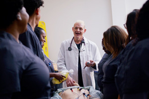 EKG instructor teaching a group of students surrounding a simulation mannequin.