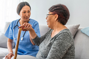 Healthcare worker wearing a stethoscope is sitting on a sofa with a patient.