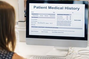 over-the-shoulder shot of a lady at a computer. The computer screen displays mock Patient Medical History information.