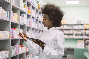 Pharmacy Tech holding an electronic tablet and examining a package of pharmaceuticals.