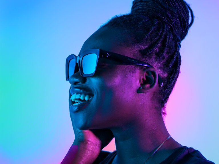 A photo of a young Black woman with braided hair smiling and wearing sunglasses.
