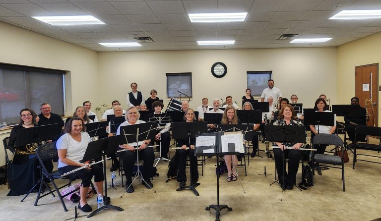 The VGCC Band consisting of approximately 27 members are smiling while sitting and holding their instruments.