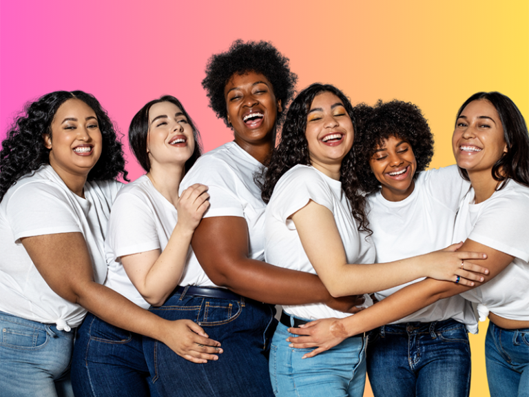 Multiethnic women in white T-shirts and blue jeans hugging each other. Credit Luis Alvarez (Getty Images), acquired via Canva Pro.