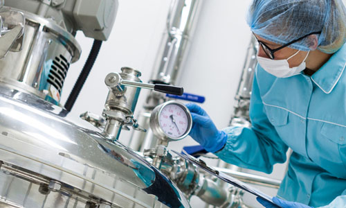 A woman wearing blue lab gear and am ask is working with lab equipment.