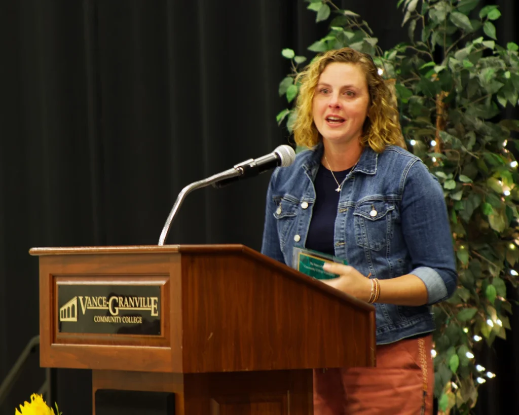 A woman speaks from behind a podium while holding an award plaque