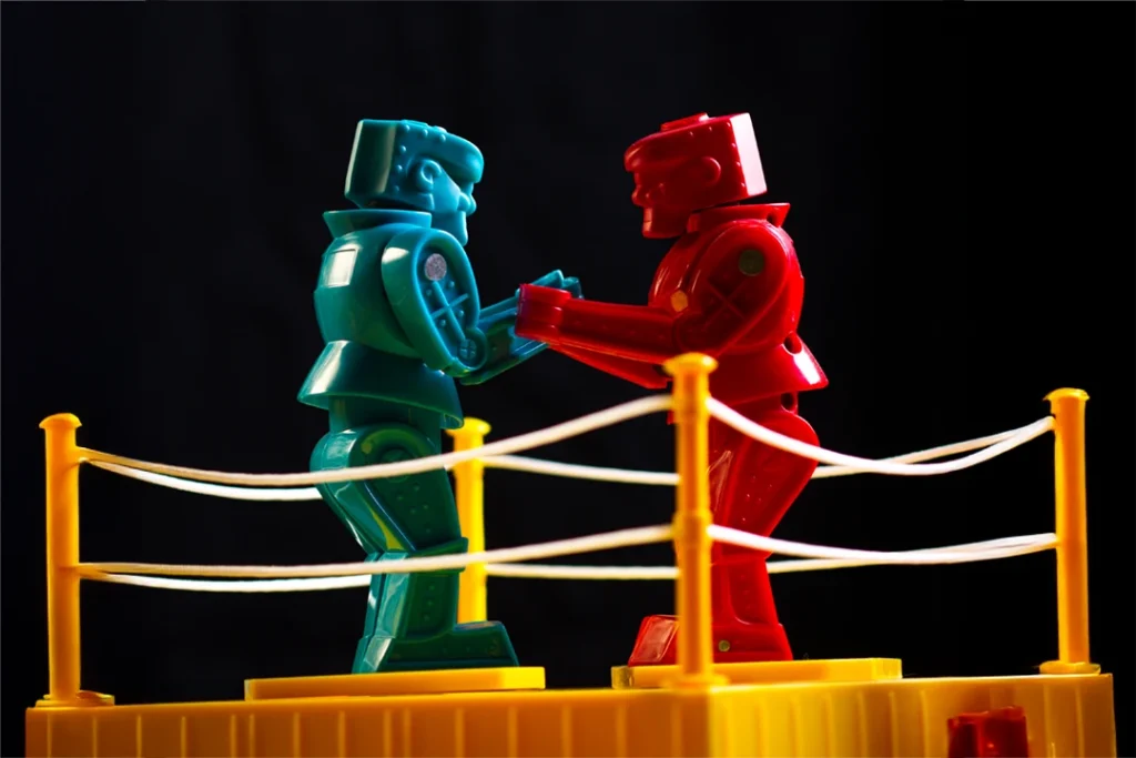 Two plastic robot figures facing off in a toy boxing ring; key visual for VGCC Drama's 2026 production of 'God of Carnage.'