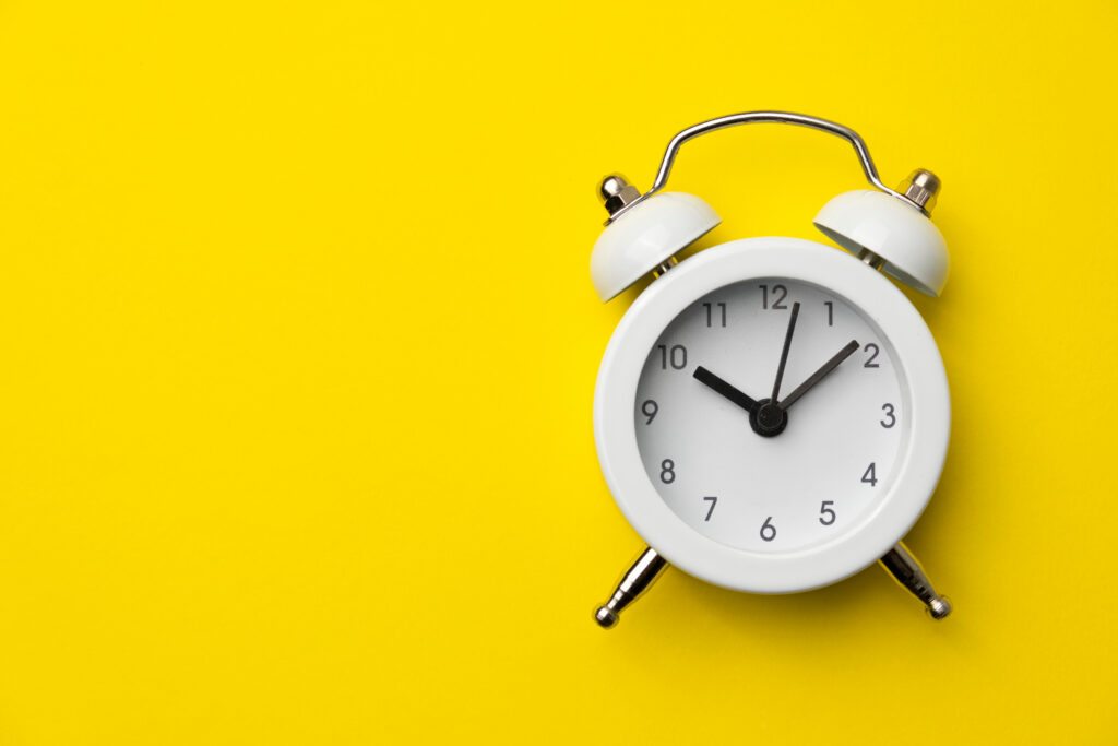 A white, old-fashioned alarm clock on a yellow background.