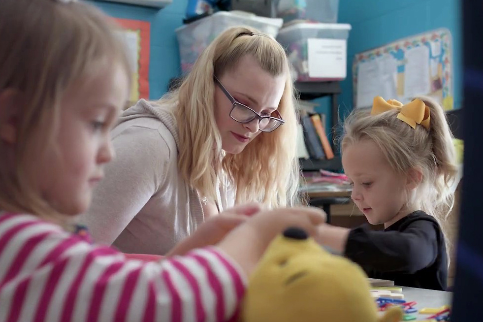 A woman helping two young children in classroom.