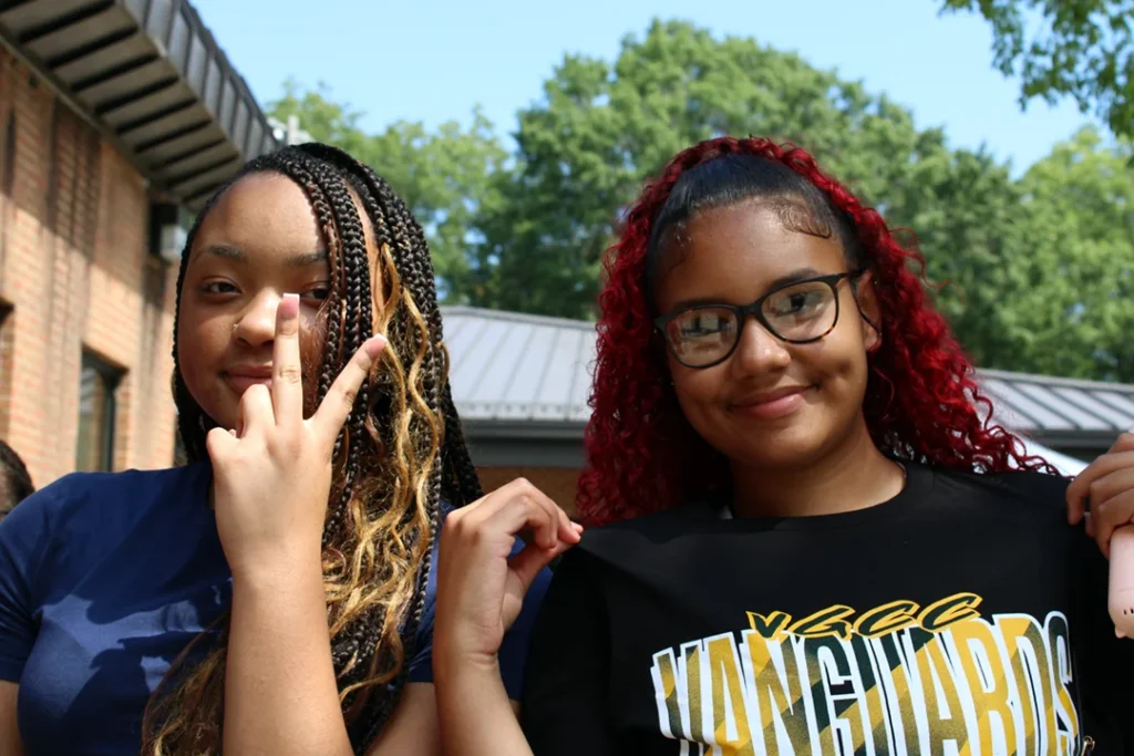 Two students standing outside. One is holding a piece sign, the other is showing off their VGCC Vanguards shirt.