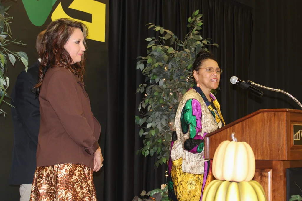 One woman watches as another speaks behind a podium