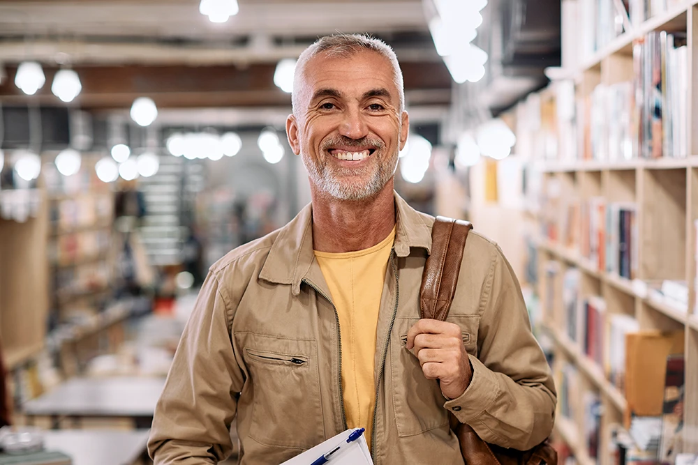 An older gentleman standing in a library, smiling.