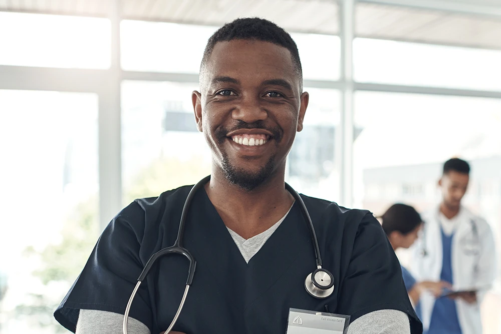 A man wearing black scrubs with a stethoscope around his neck.