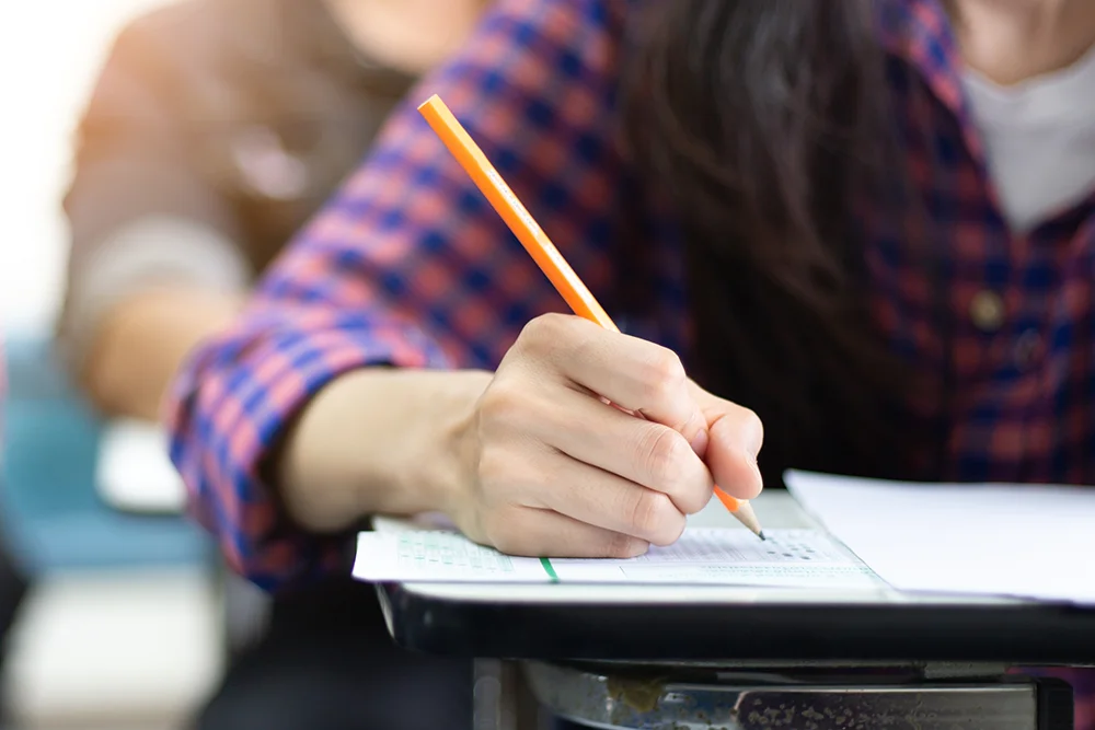 A student filling in a bubble on a paper test sheet representing.