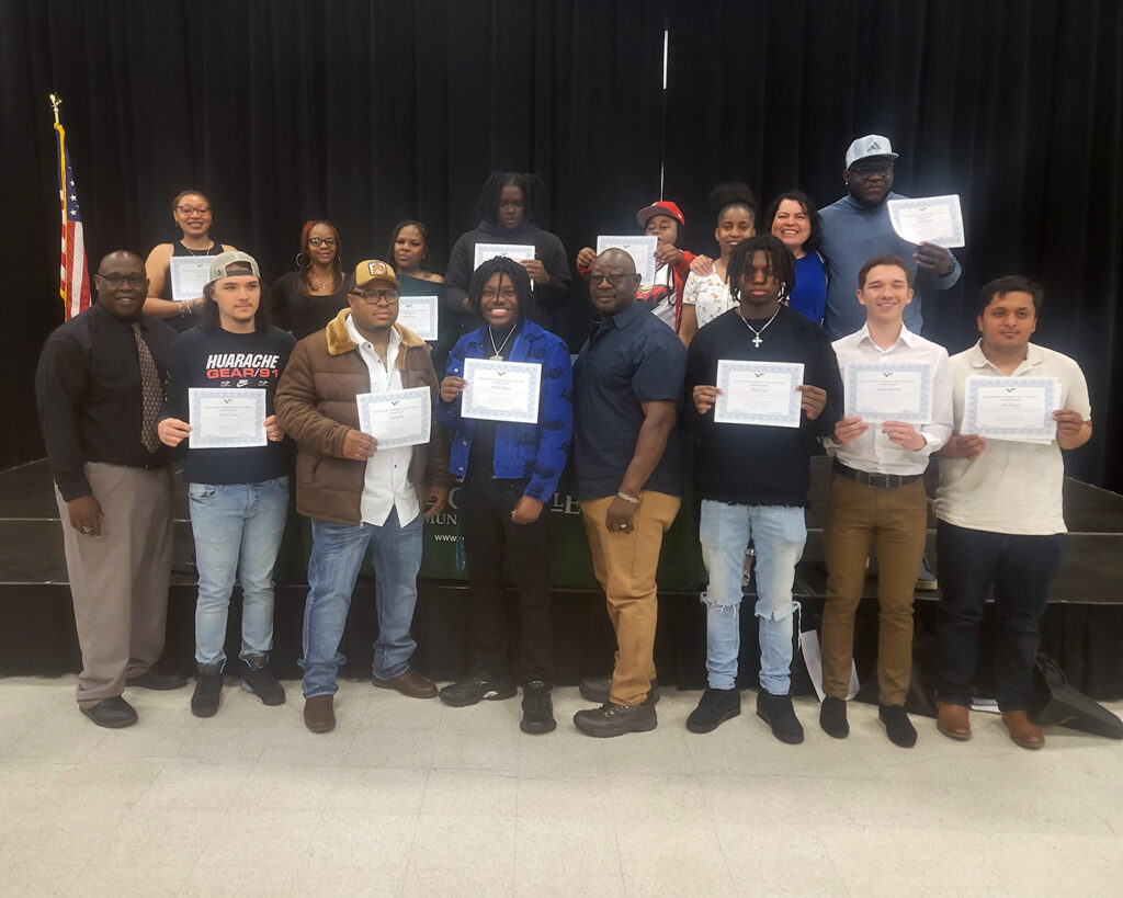 A group of about 14 students reflecting different ages, races, and genders holds up certificates in celebration