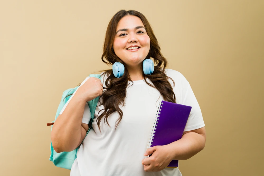 A woman wearing a white shirt with a blue book bag and a smile.
