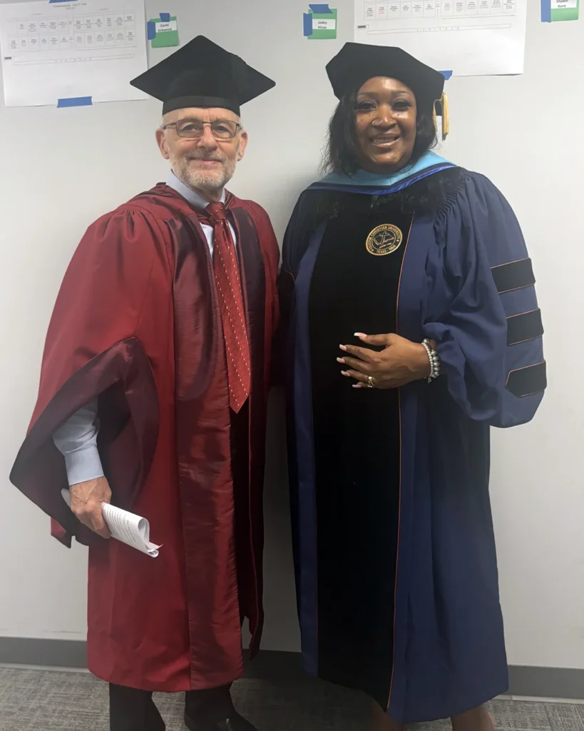 A man in red academic robes stands beside a woman wearing doctoral regalia