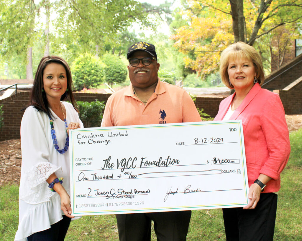 A man stands between two women as they hold a large presentation check, which is labeled 'Jovan Q Steed Annual Scholarships.'