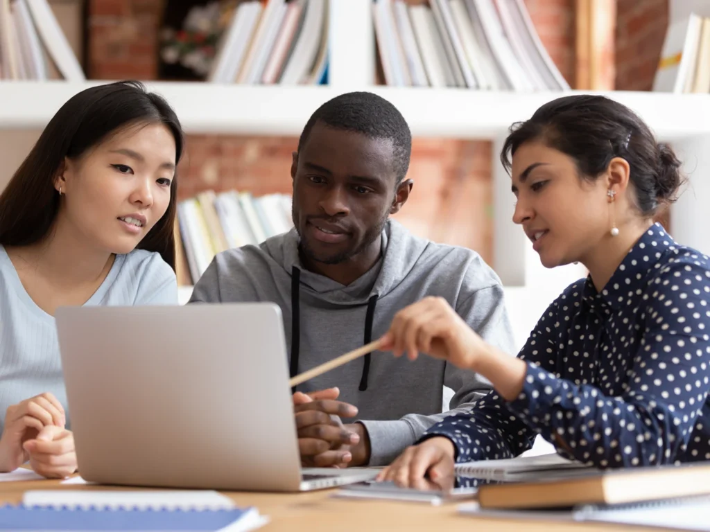 Multiethnic diverse students sit at desk look at laptop screen working together at school project [Shutterstock ID 1439273117]