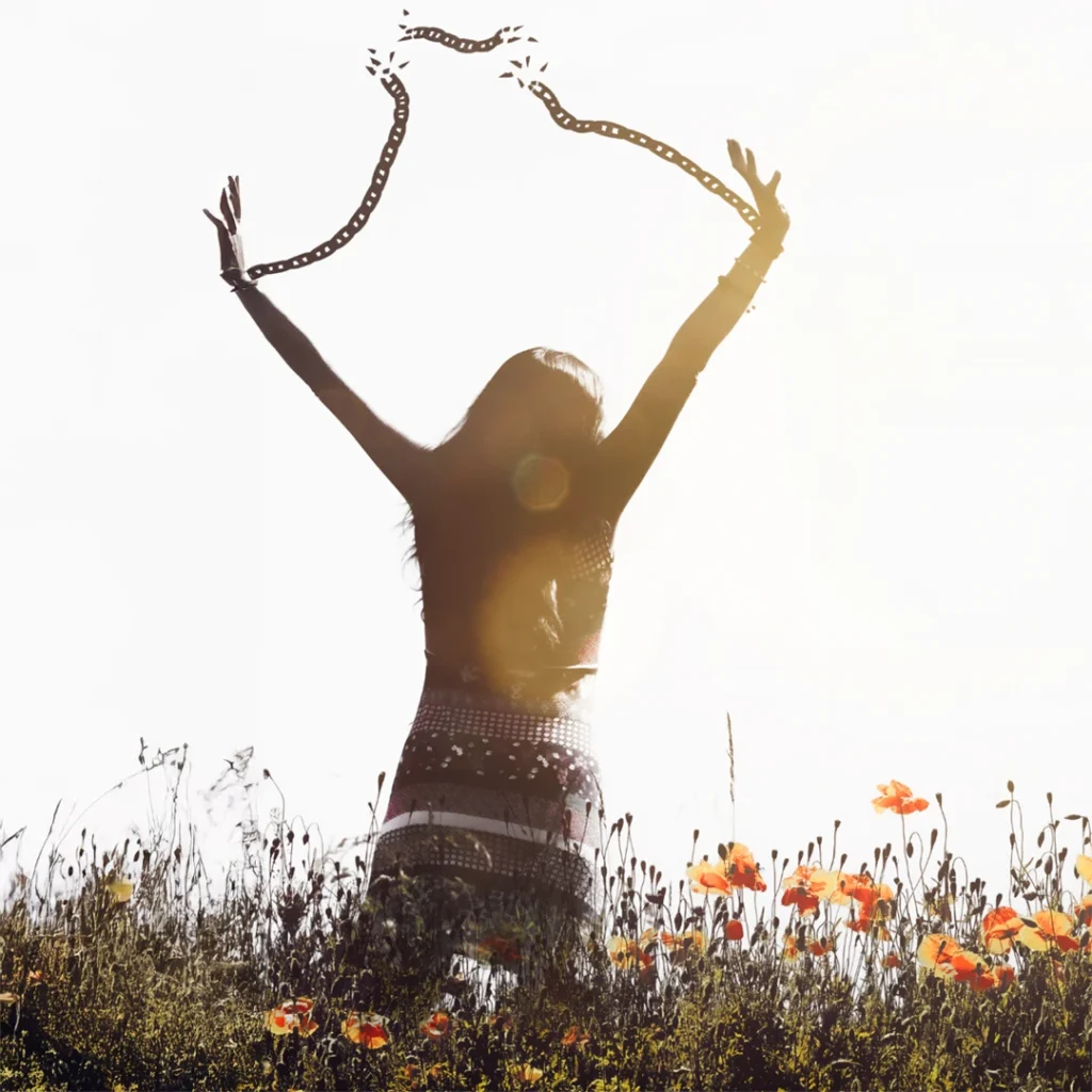 Stock photo: High-contrast image of a woman standing in a field of flowers, her arms extended as to break a chain that had bound her.