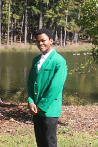 Elijah Hanks wearing a green VGCC ambassador's coat outside in front of the main campus pond.