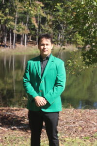 Emanuel Gutierrez wearing a green VGCC ambassador's coat outside in front of the main campus pond.