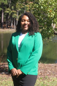 Felicia Jones wearing a green VGCC ambassador's coat outside in front of the main campus pond.