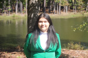 Lynna Mariano wearing a green VGCC ambassador's coat outside in front of the main campus pond.