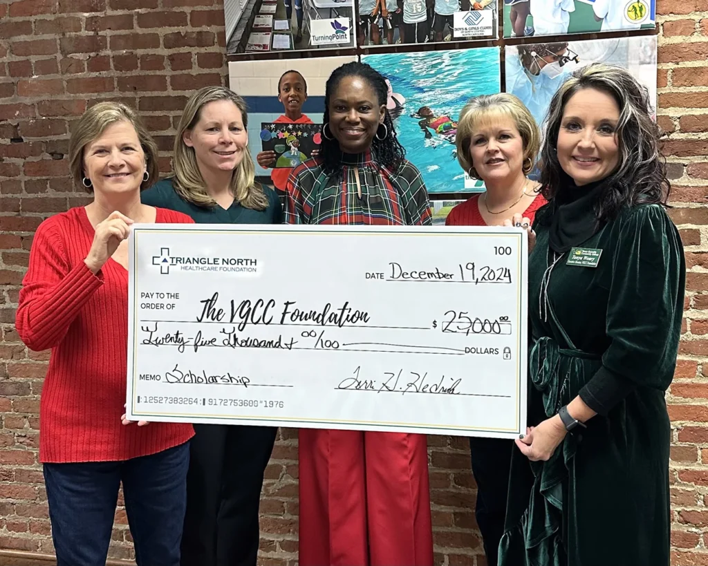 Five women representing the Triangle North Healthcare Foundation and VGCC Foundation pose with a large presentation check
