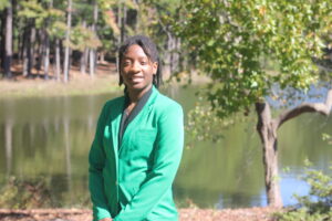 Victoria Sema wearing a green VGCC ambassador's coat outside in front of the main campus pond.