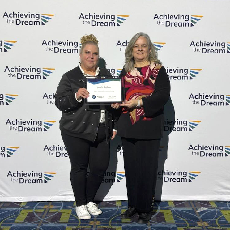 Two women accept a certificate of recognition on behalf of their community college