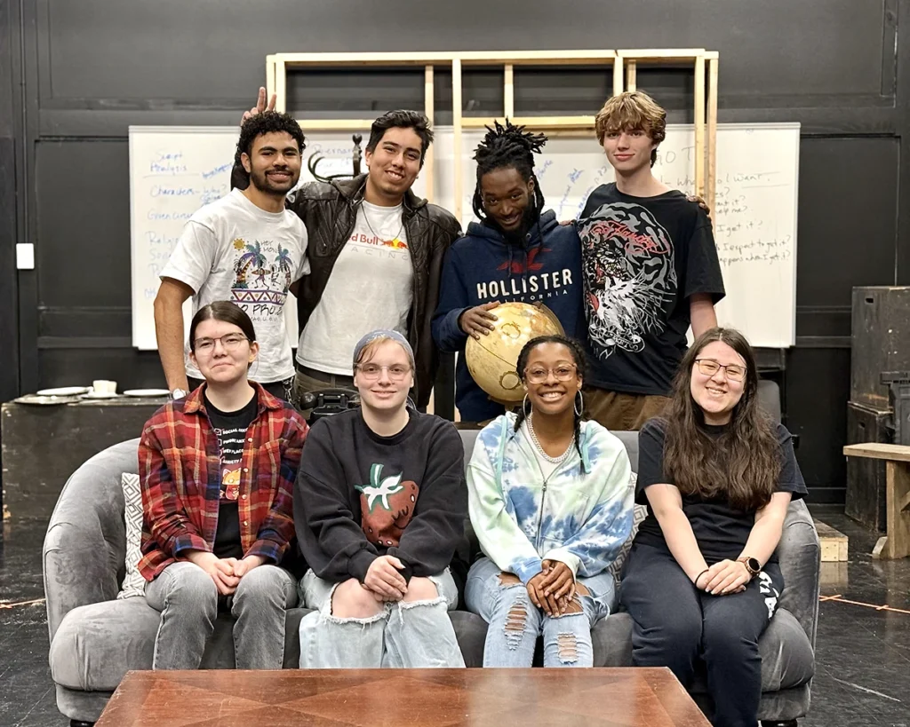 Eight diverse college students gathered for a group photo on a theatrical stage