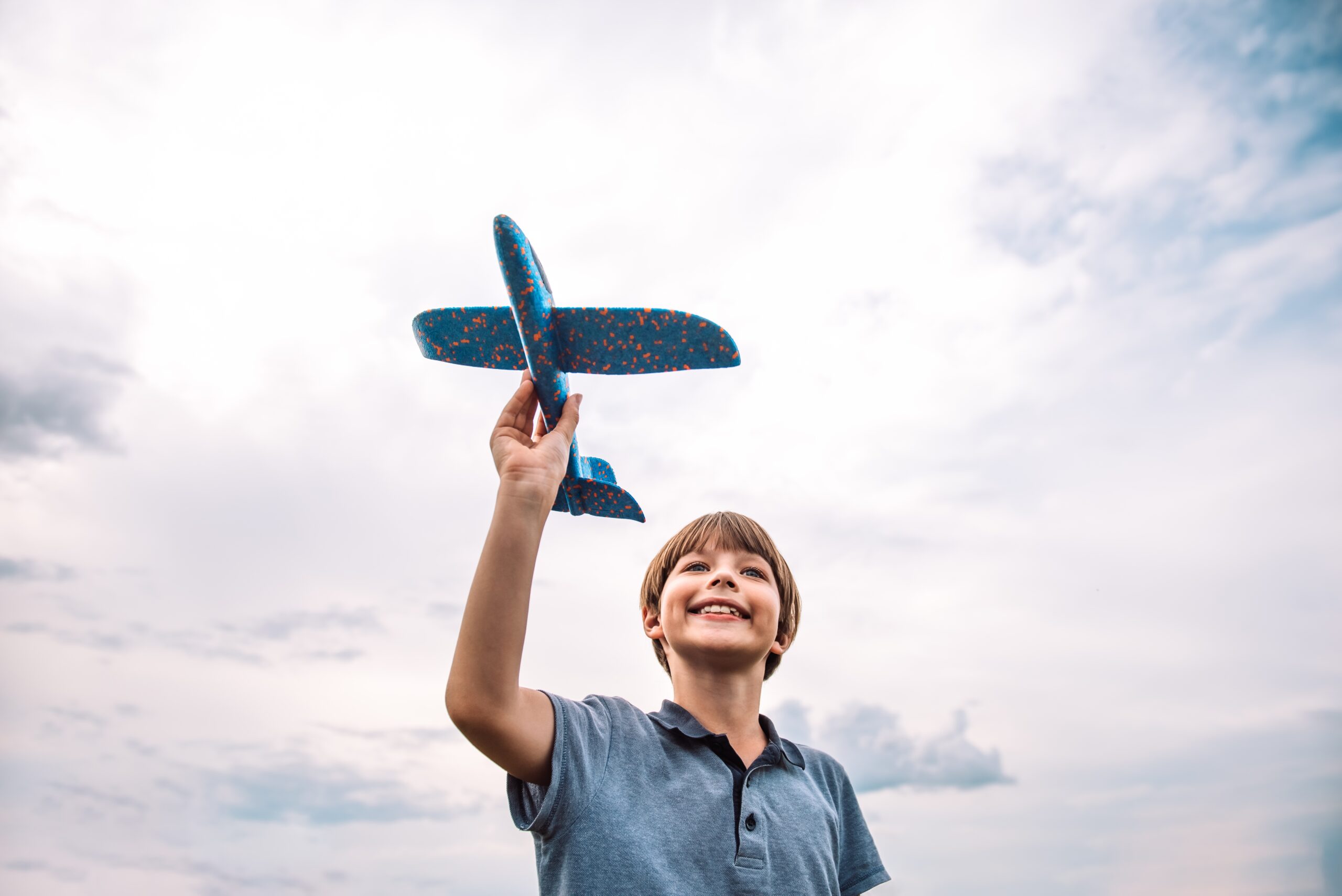 A young boy playing with a model airplane with the sky in the background.