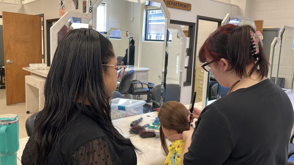 Two CCP Cosmetology Students combing the hair of a mannequin head.