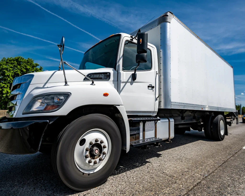 White industrial carrier truck with long box trailer driving on a highway [CDL-B]