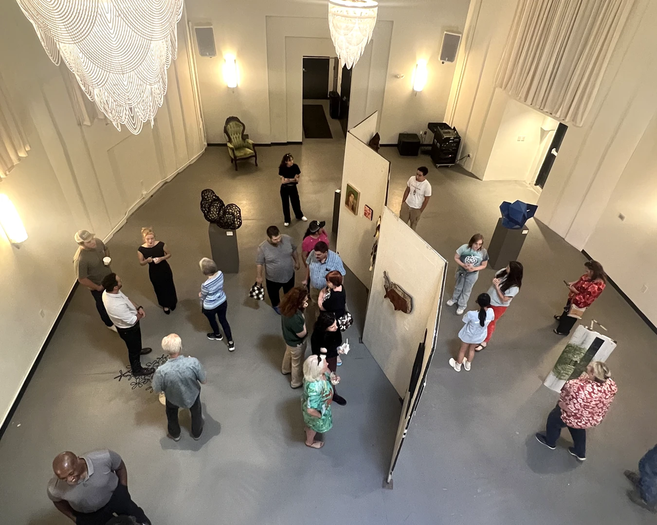An overhead shot of about 20 people in an event space, walking around to view a gallery of sculptures and mounted paintings