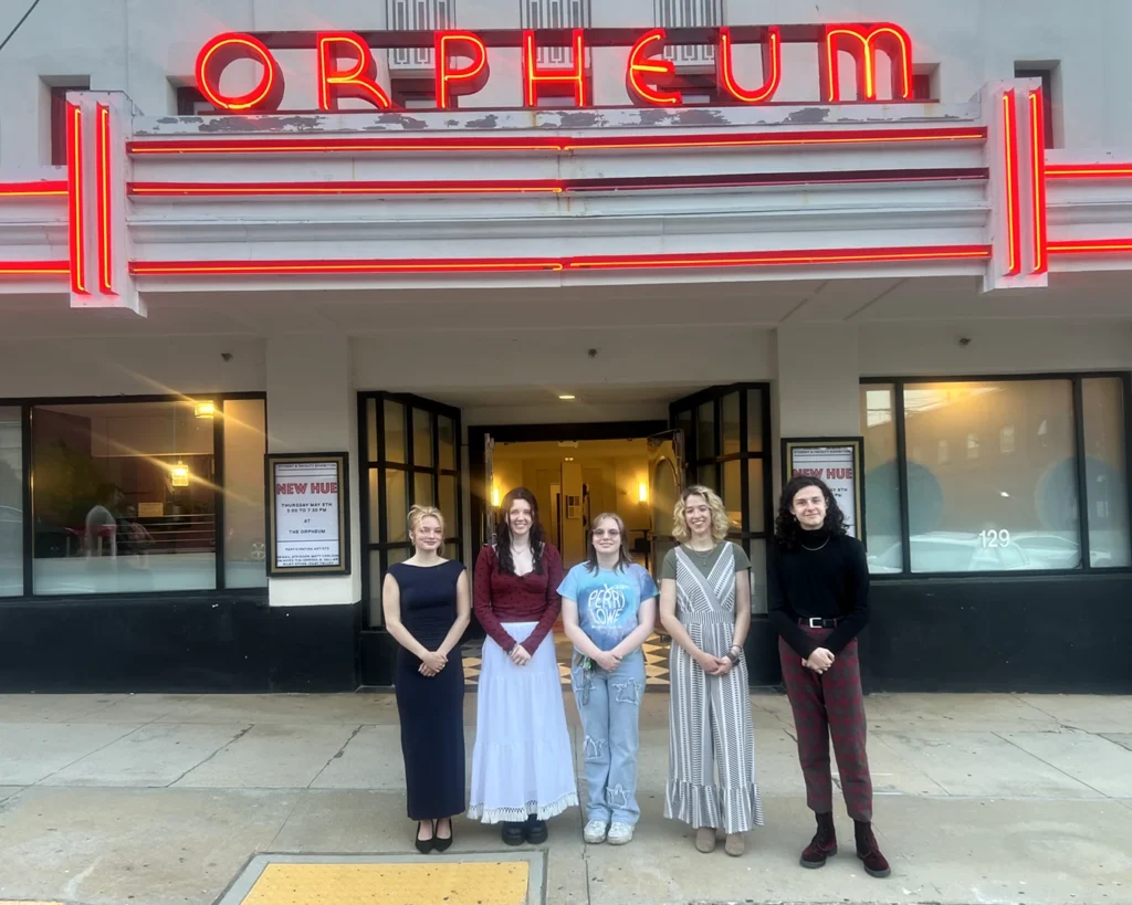Five college students stand under a red neon marquee which reads 'Orpheum' [New Hue]