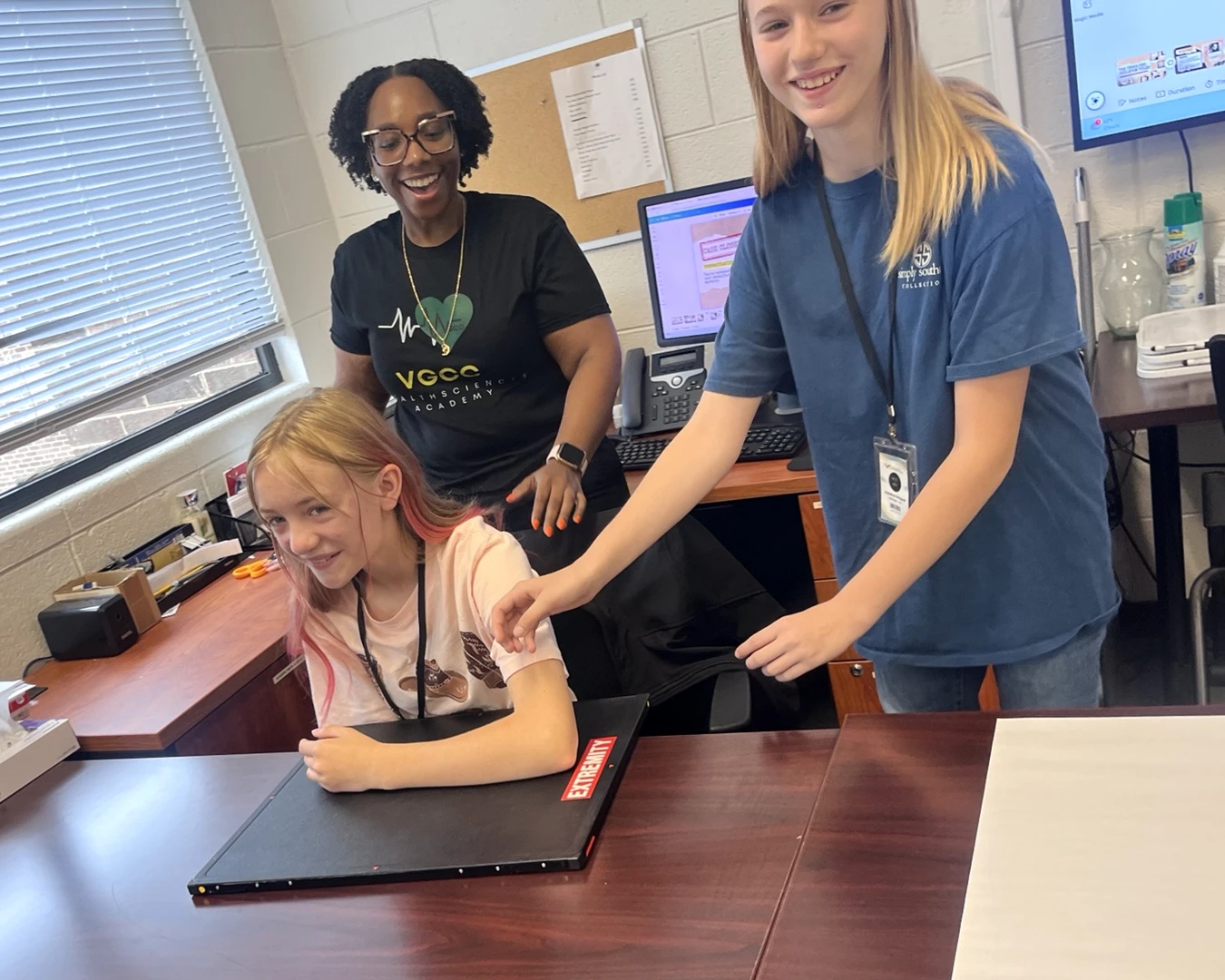 A woman and two preteen girls laugh together in a health sciences classroom
