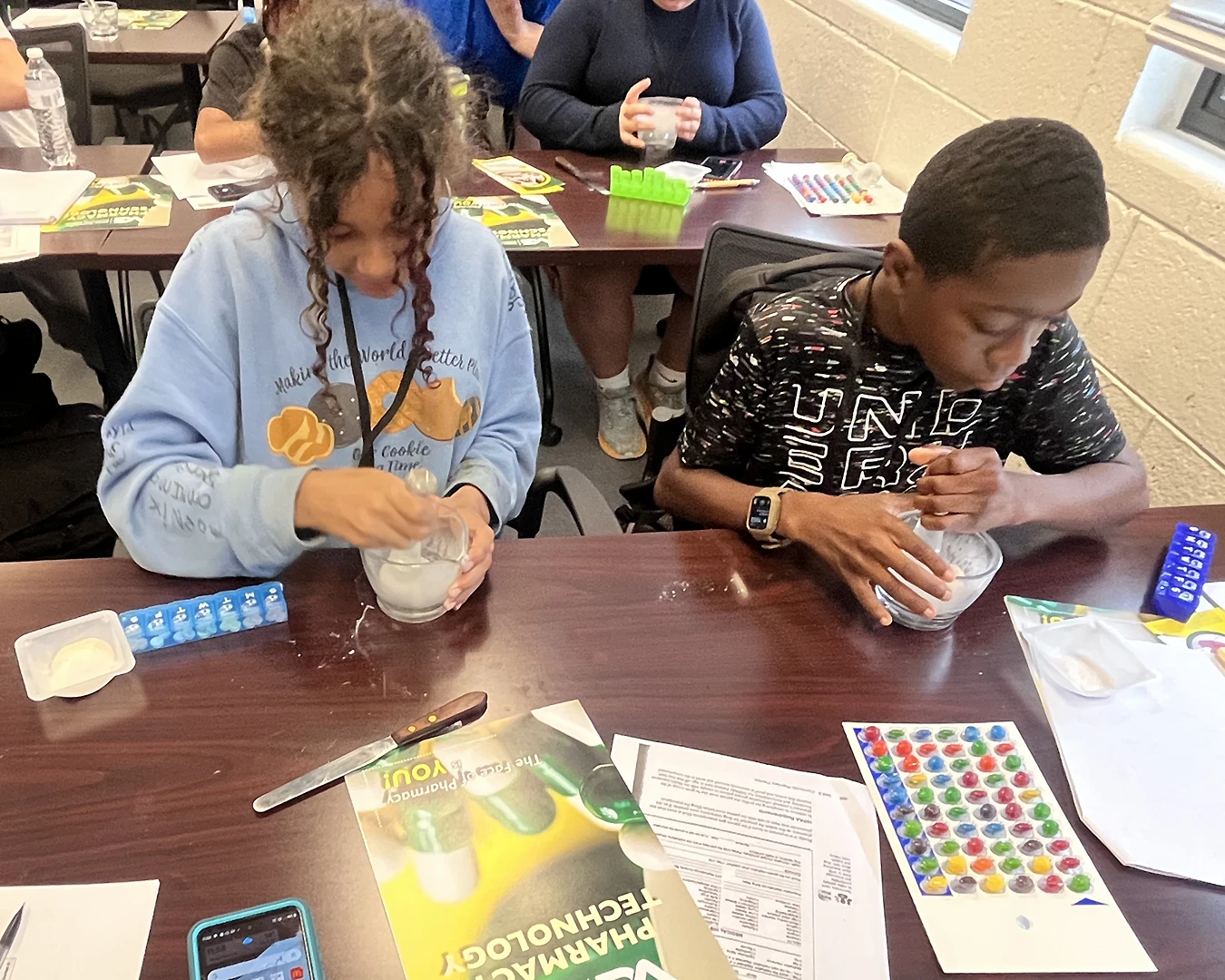 Two middle school students crush candy using a mortar and pestle.