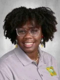 Yearbook-style portrait of Beginning Teacher Oneisha Leonard-Henry, a young woman with afro-style hair, glasses, and a toothy smile.