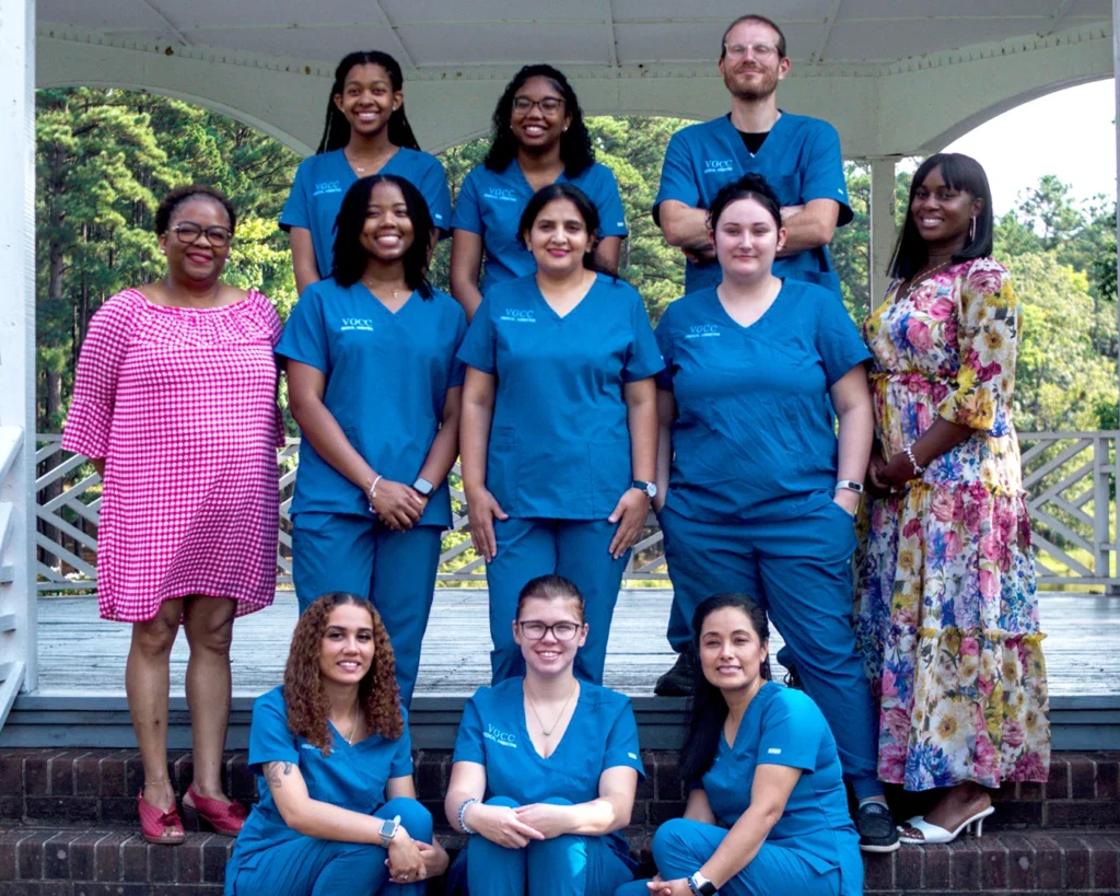 Nine Medical Assisting students in blue scrubs stand in an outdoor gazebo with two female instructors.