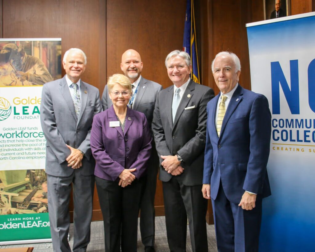 Four men and one woman, all wearing business suits, stand between two branded banners which read 'Golden LEAF Foundation' and 'NC Community Colleges: Creating Success.'