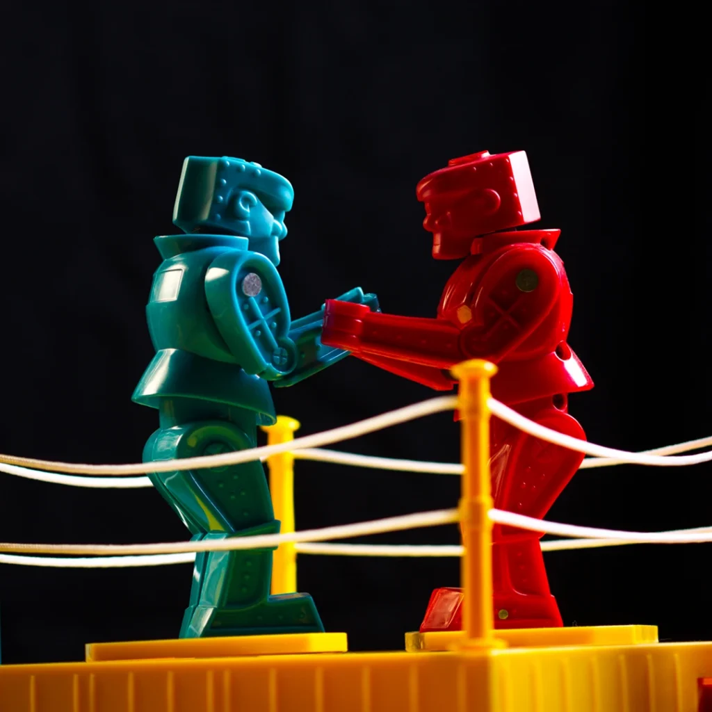 Two plastic robot figures facing off in a toy boxing ring; key visual for VGCC Drama's 2026 production of 'God of Carnage.'