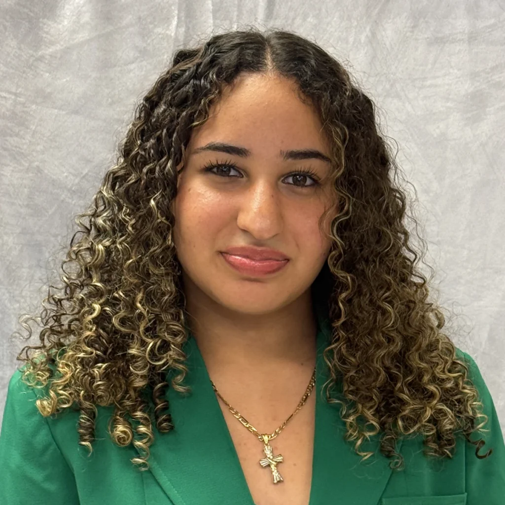 Photo of Ann Sheteiwy, a young woman with curly hair wearing a green VGCC student ambassador's blazer.