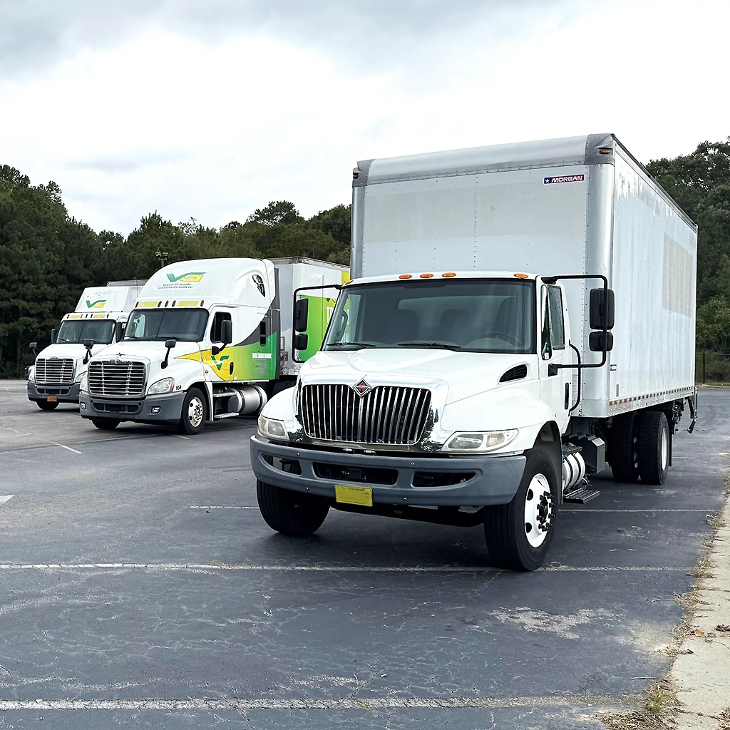 Three commercial trucks of different sizes parked in a row in a large lot; two of the trucks have Vance-Granville Community College branding, while the third is solid white.