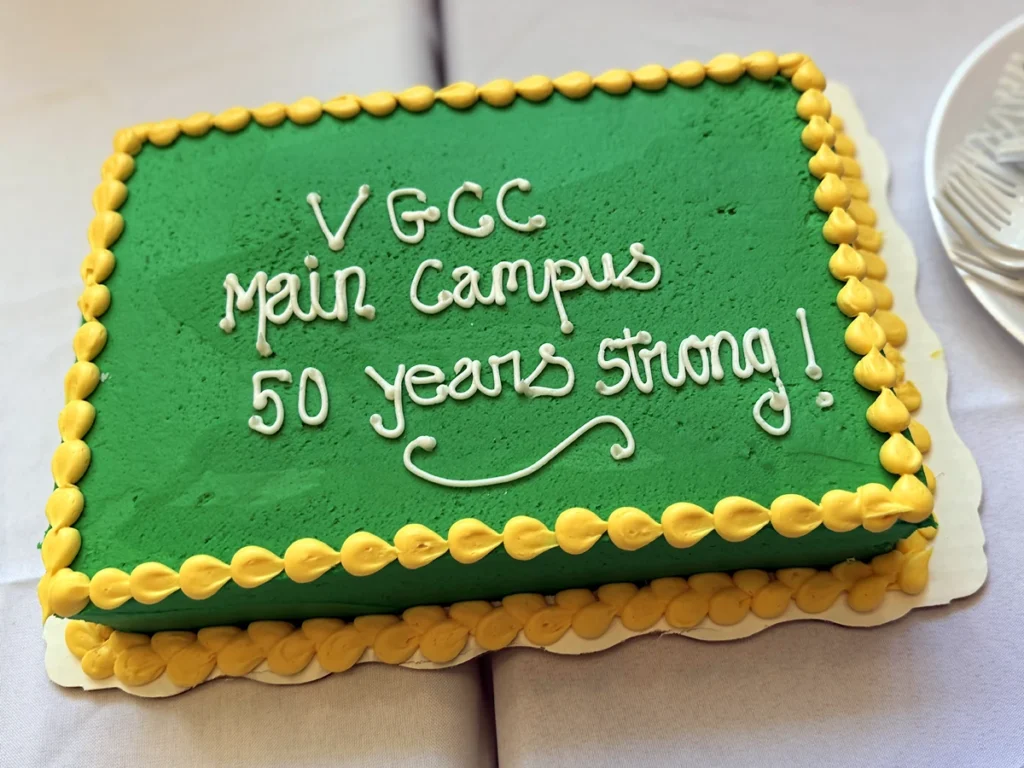 A green frosted sheet cake with yellow trim and white script writing: 'VGCC Main Campus 50 Years Strong!'