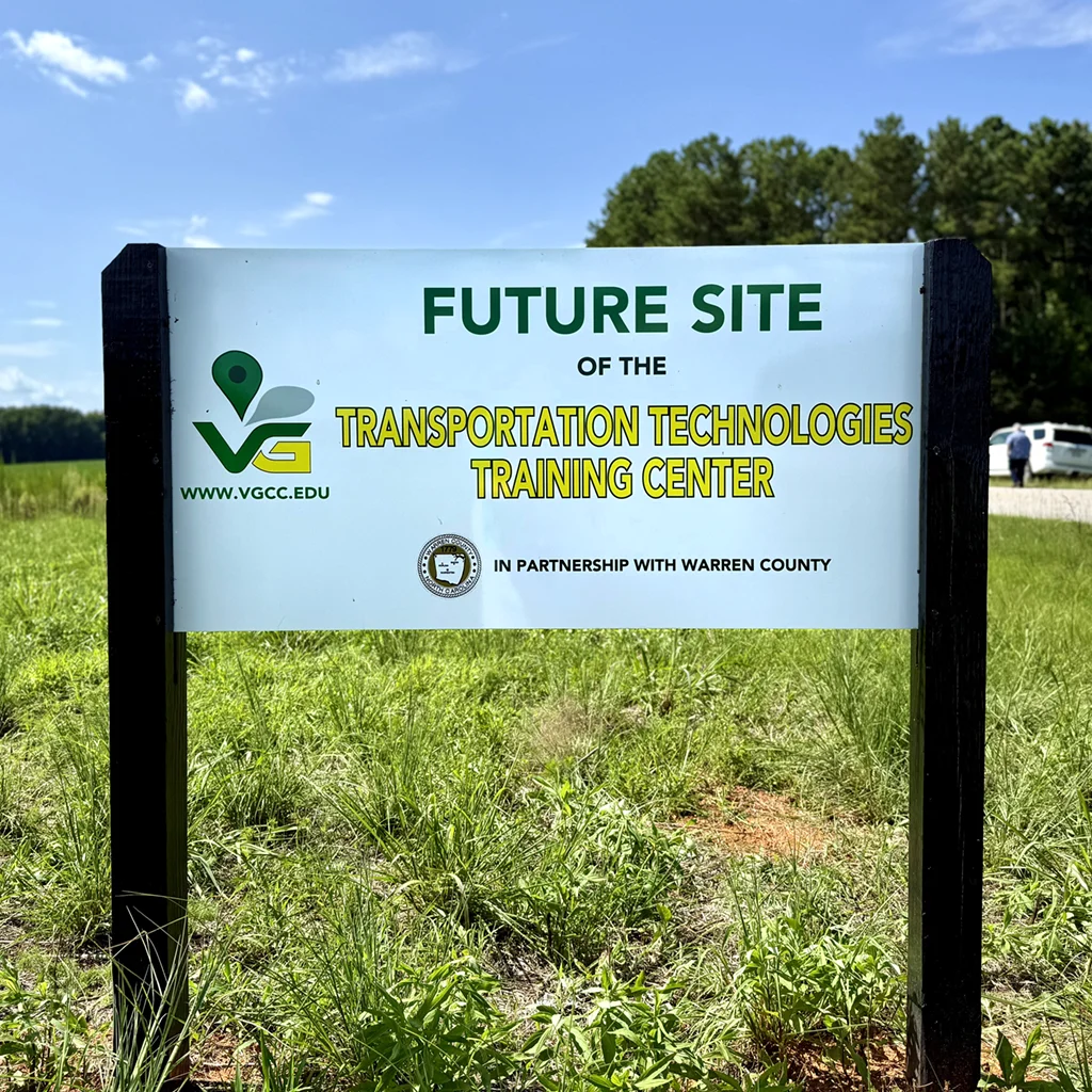 Mounted sign in a grassy field beside a rural road: 'Future Site of the Transportation Technologies Training Center, in partnership with Warren County, www.VGCC.edu.'