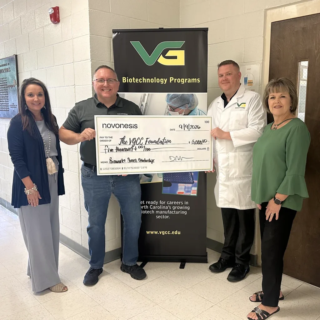 Four adults, one wearing a white lab coat, stand in front of a banner that says 'VG Biotechnology Programs' while holding a large presentation check from Novonesis.