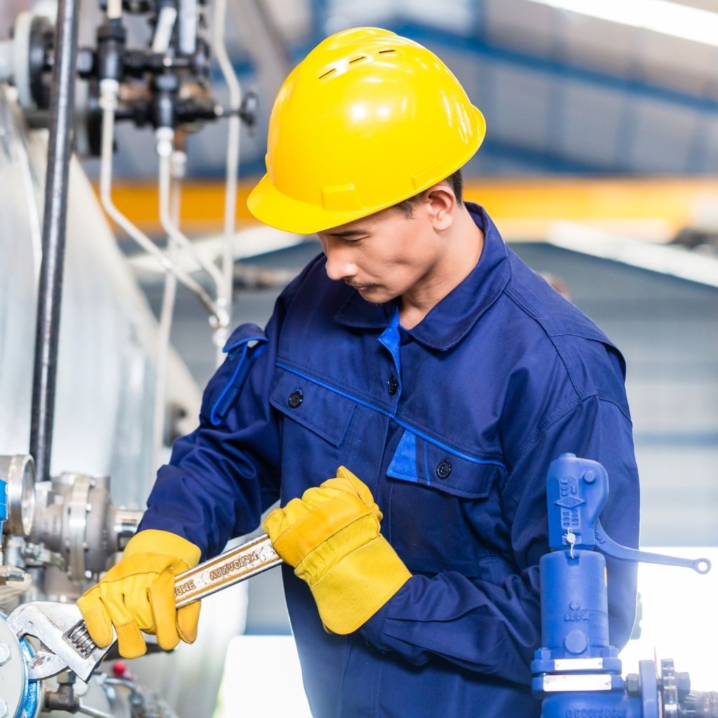 Male-presenting technician performing machine maintenance with wrench in a factory setting [Shutterstock 258812027].